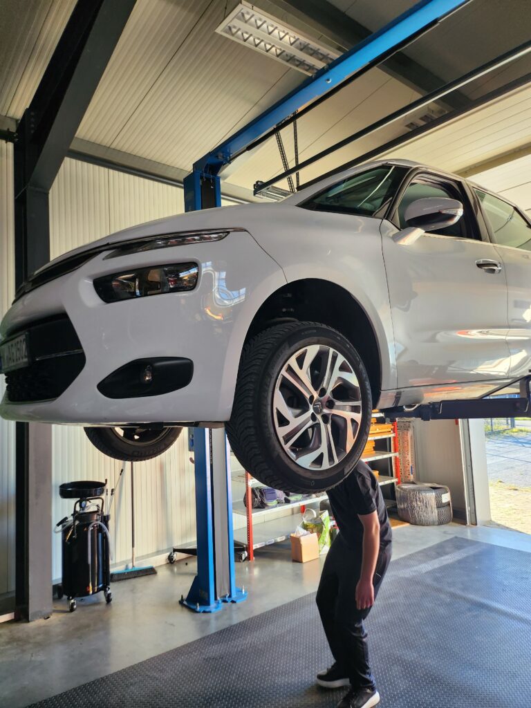 Kunde inspiziert sein Fahrzeug unter einer Hebebühne von Autoselbsthilfe Lüneburg
